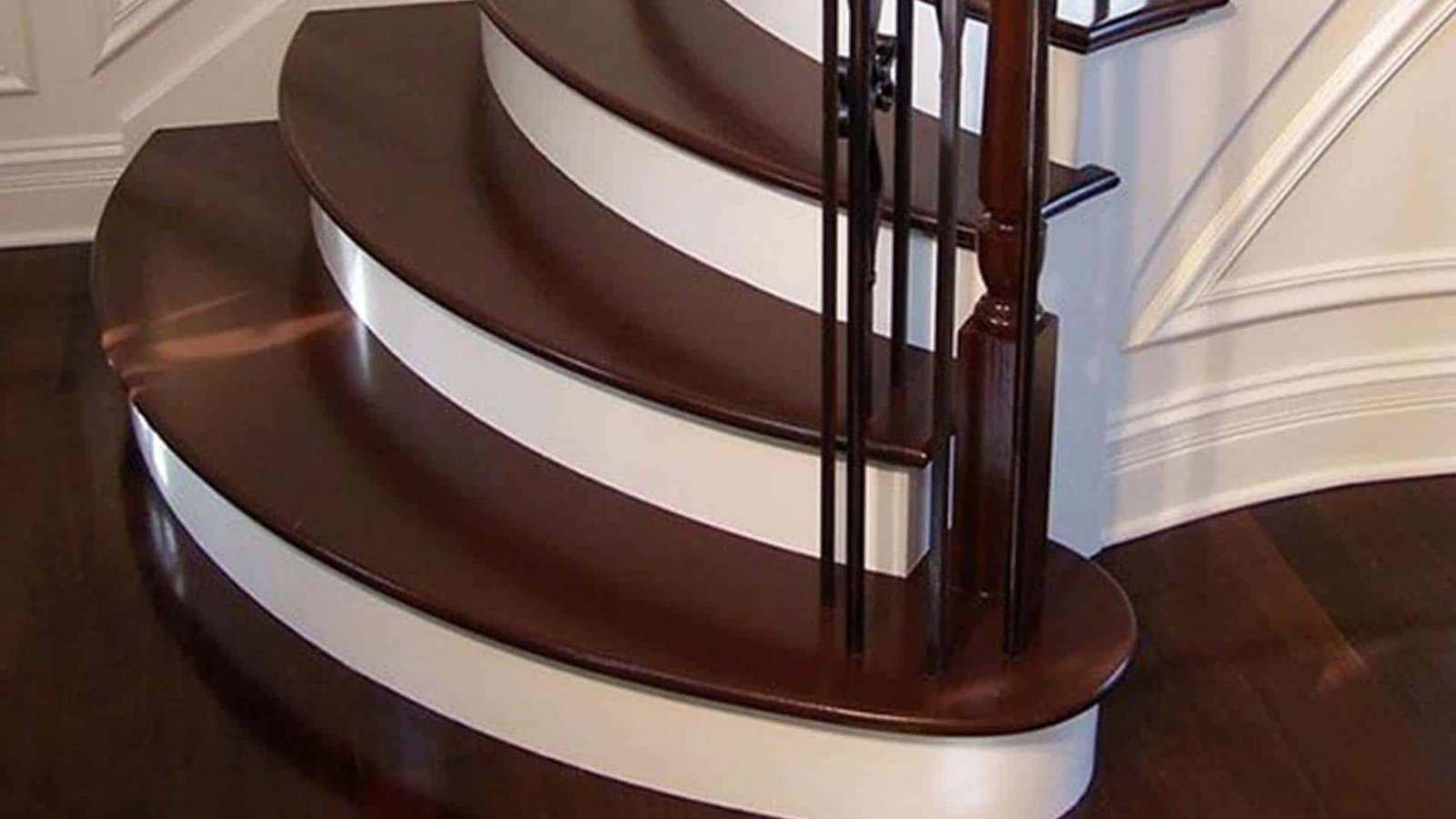 Curved staircase with dark hardwood treads, white risers, and black iron balusters
